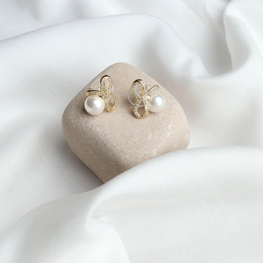 QuinShine luxury pearl earrings for women with gold and crystal bow design on a stone display