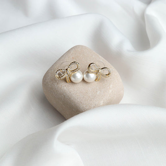 QuinShine luxury pearl earrings for women with gold bow and white pearls on a beige stone