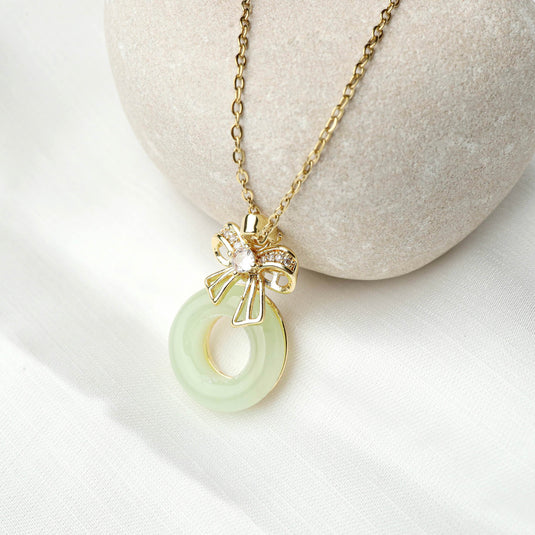 Gold chain necklace with unique gemstone jewelry pendant featuring pale green circular stone and decorative bow