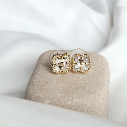 QuinShine unique gold stud earrings with intricate floral design on soft beige stone and white fabric background