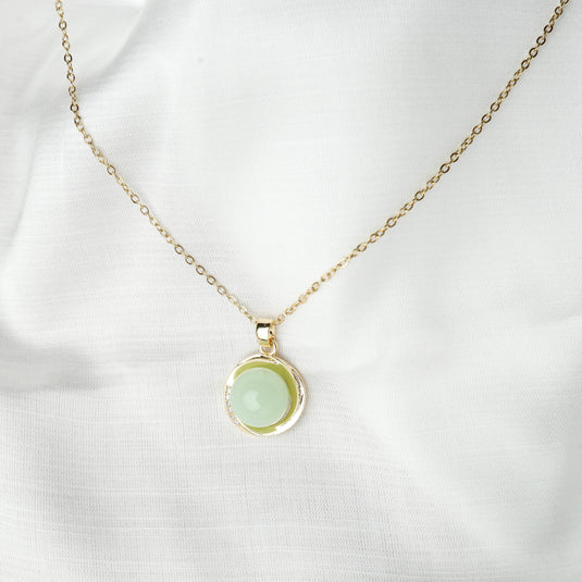 QuinShine serenity circle necklace with gold chain and light green circular pendant on white fabric