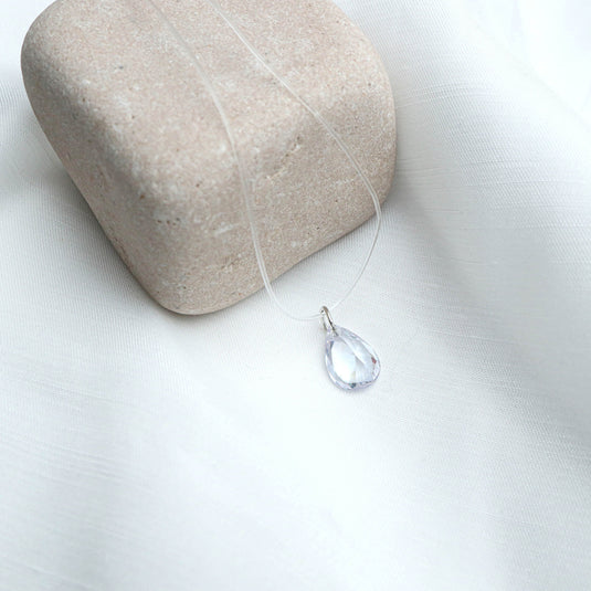 QuinShine crystal drop necklace with clear teardrop pendant on transparent chain displayed on beige stone