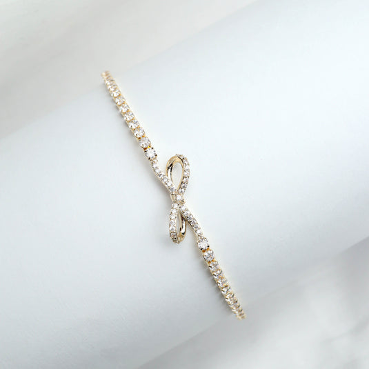Delicate gold bracelet for women with a bow design and sparkling stones on a white display