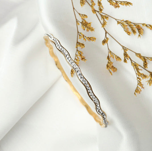 Elegant gold and silver wave bracelet with sparkling crystals displayed on white fabric with dried floral accents