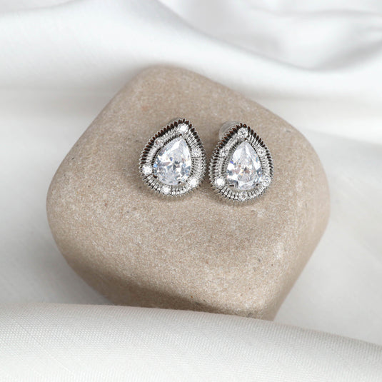 Elegant silver stud earrings with pear-shaped clear gemstones displayed on a smooth stone