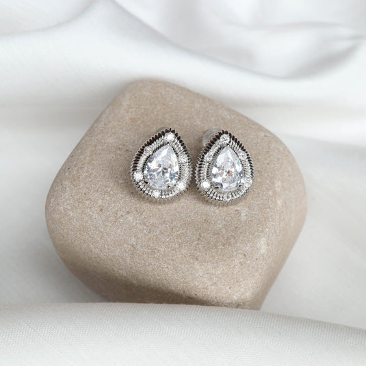 Elegant silver stud earrings with teardrop shaped clear stones on a smooth beige stone