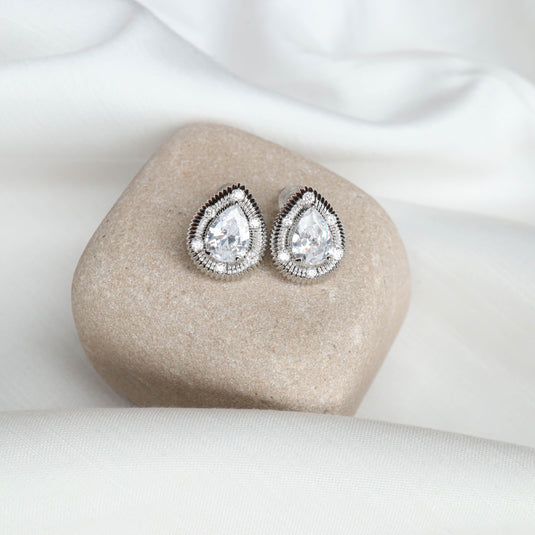 Elegant silver stud earrings with teardrop-shaped clear stones on beige stone display