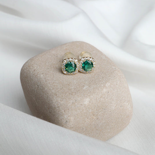 QuinShine emerald crown stud earrings with green gemstones and surrounding clear crystals on beige stone