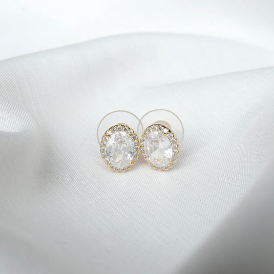 QuinShine aura oval stud earrings with sparkling clear stones and gold trim on white fabric