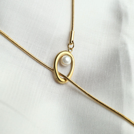 Gold baroque pearl lariat necklace with oval pendant on white fabric background