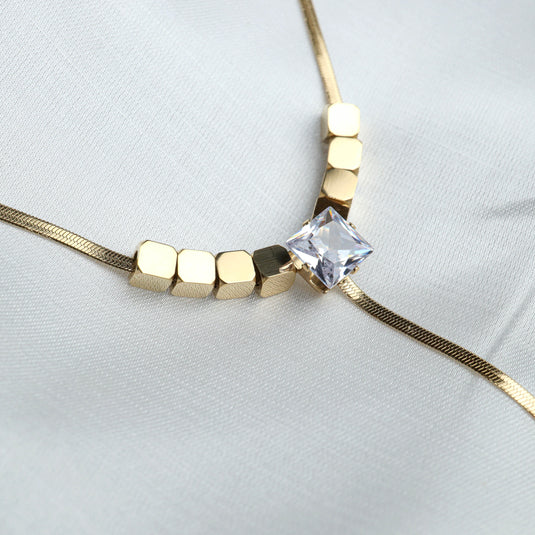 Diamond pendant lariat necklace with gold cubic beads and square clear diamond on white fabric