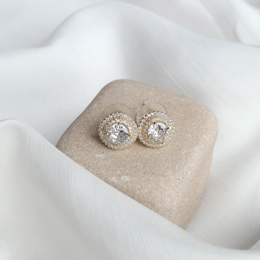 QuinShine elegant gold halo earrings with sparkling clear stones on beige stone and white fabric