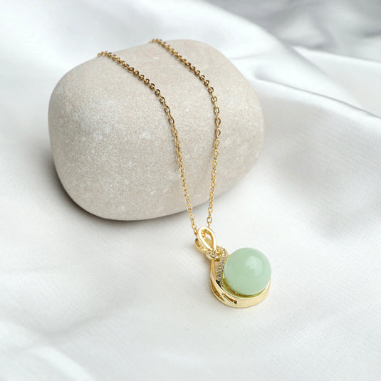 QuinShine jade pendant necklace with gold chain and light green round jade stone on white fabric
