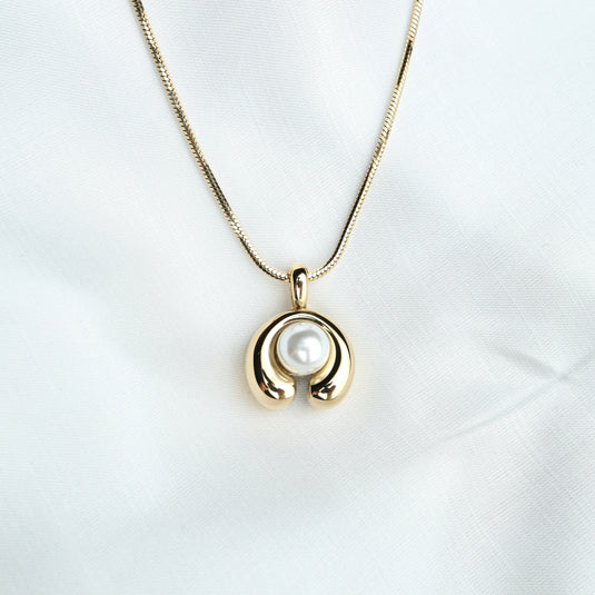 Gold modern pearl pendant necklace with a unique crescent design featuring a central pearl