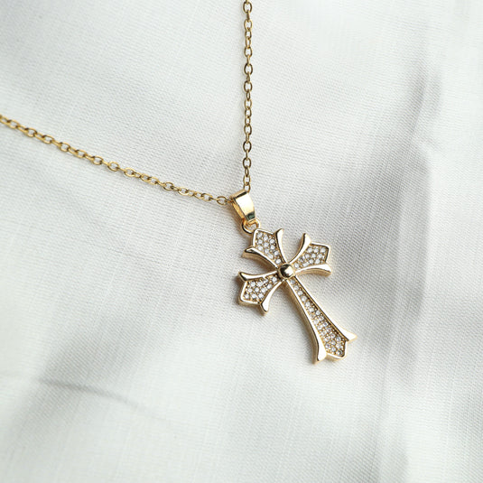 Gold pavé cross necklace with delicate chain and sparkling stone details on white fabric