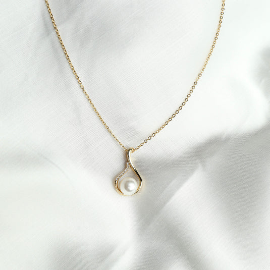 Elegant Gold Pavé Pearl Necklace with a delicate gold chain and pearl pendant on white fabric