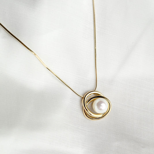 Elegant gold pearl necklace with a single large pearl encased in a twisted gold pendant
