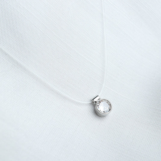 Elegant gold transparent chain necklace with a clear round crystal pendant on white fabric