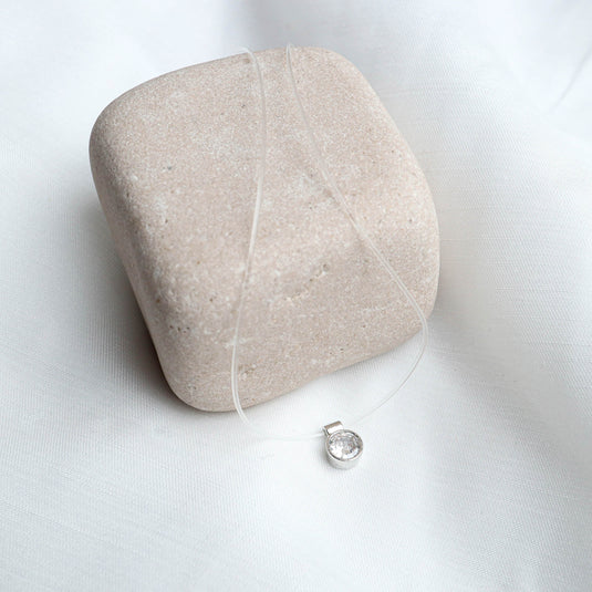 QuinShine gold transparent chain necklace with a clear pendant displayed on a beige stone and white fabric