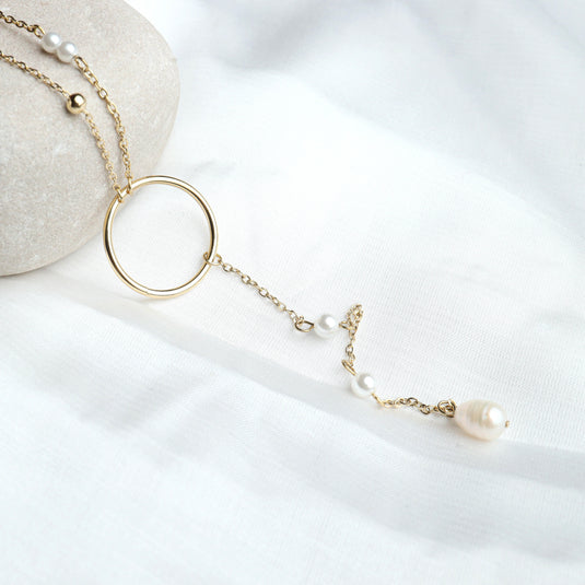 QuinShine long chain lariat necklace in gold with pearls and circular pendant on white fabric