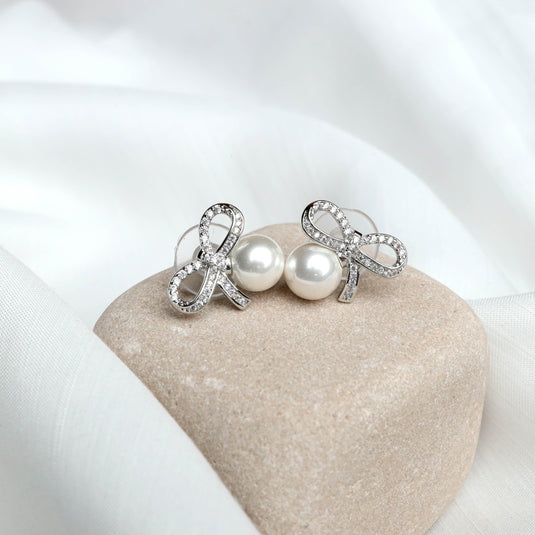 QuinShine loop design earrings with sparkling crystals and pearl studs on beige stone display