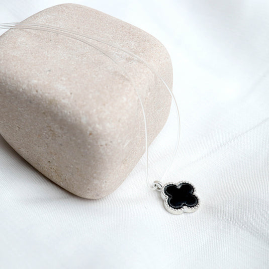 Midnight Clover necklace with black clover pendant on silver chain displayed on beige stone