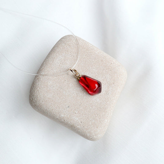 QuinShine elegant sheer necklace with a red pendant on a clear string displayed on a beige stone