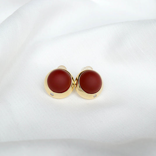 Scarlet sphere stud earrings with gold setting and small diamond detail on white fabric background