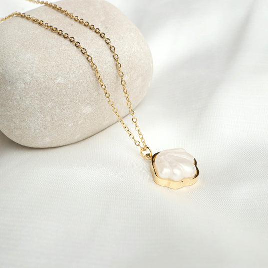 Elegant seashell pendant jewelry with gold chain resting on white fabric and smooth stone