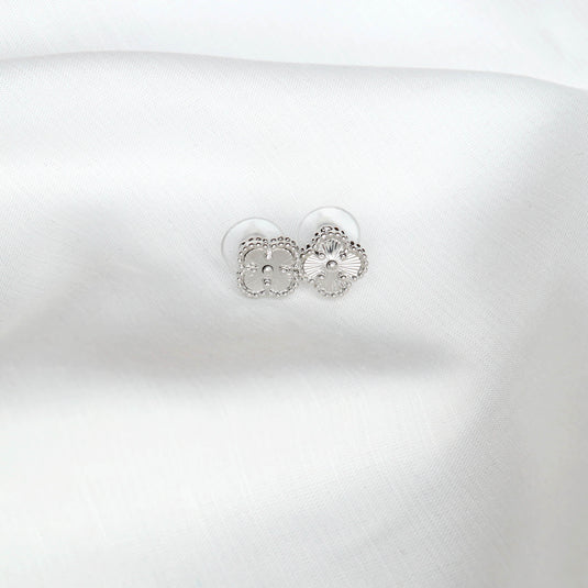 QuinShine delicate silver four leaf clover earrings with intricate detailing on white fabric
