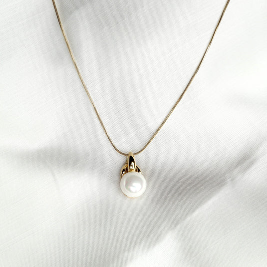 Elegant solitaire pearl pendant on a delicate gold chain displayed on white fabric