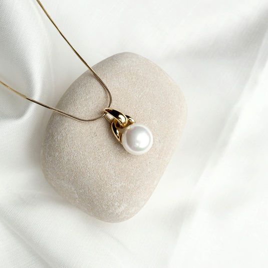 Elegant solitaire pearl pendant with gold setting displayed on a beige stone by QuinShine