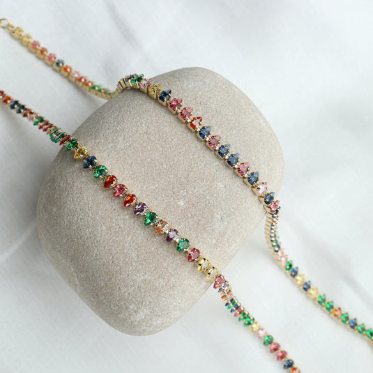 QuinShine tennis necklace colorful stones with multicolored gems set in gold displayed on a smooth stone