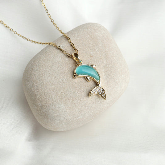 Turquoise Stone Dolphin Necklace with gold chain displayed on a smooth beige stone background
