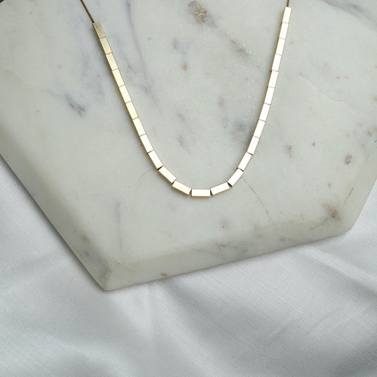 Elegant gold necklace featuring unique square bead jewelry design on marble background