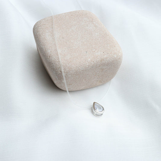 QuinShine crystal dewdrop necklace with a clear teardrop pendant on a transparent cord displayed on a beige stone
