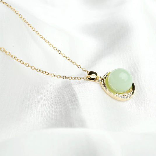 QuinShine serenity circle necklace with gold chain and light green gemstone pendant on white fabric
