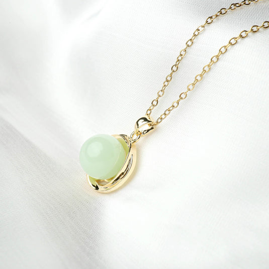 QuinShine serenity circle necklace featuring a gold chain with a green sphere pendant on white fabric