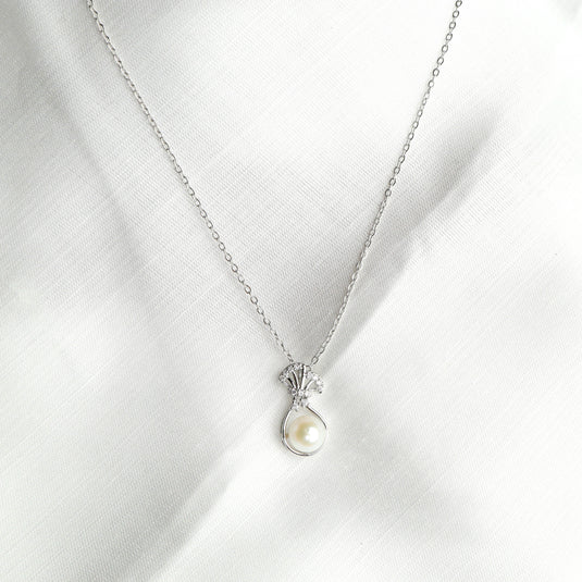 Elegant Venus shell necklace with silver chain and pearl pendant on white fabric background