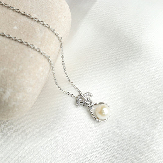 Venus shell necklace with silver chain and pearl pendant resting on white fabric and stone