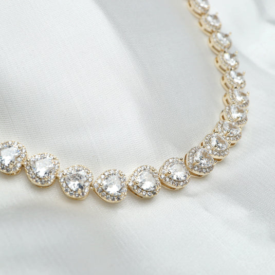 Elegant white gemstone heart necklace with gold settings displayed on white fabric background