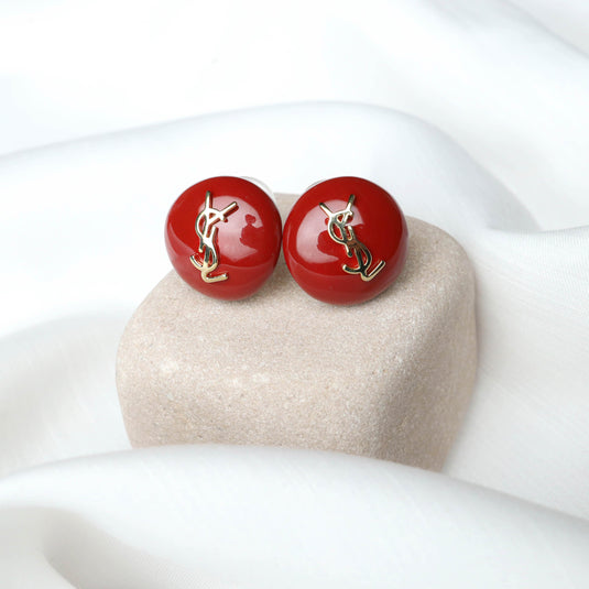 QuinShine red domed earrings for women with gold logo detail on beige stone and white fabric background